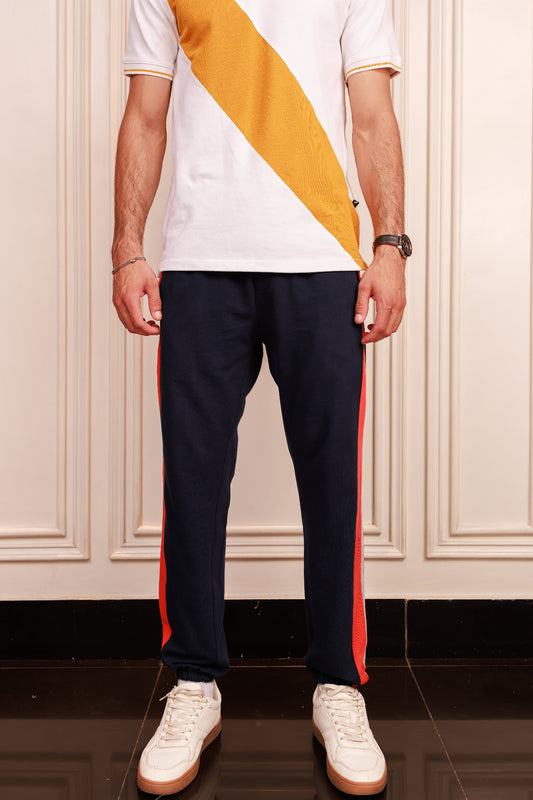 Person wearing a white shirt with a yellow stripe and navy pants with red side panels, standing indoors.