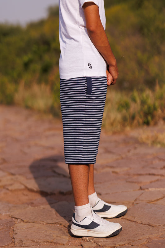 Person wearing a white t-shirt, blue striped shorts, and white sneakers on a stone path with grass in the background.