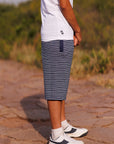 Person wearing a white t-shirt, blue striped shorts, and white sneakers on a stone path with grass in the background.