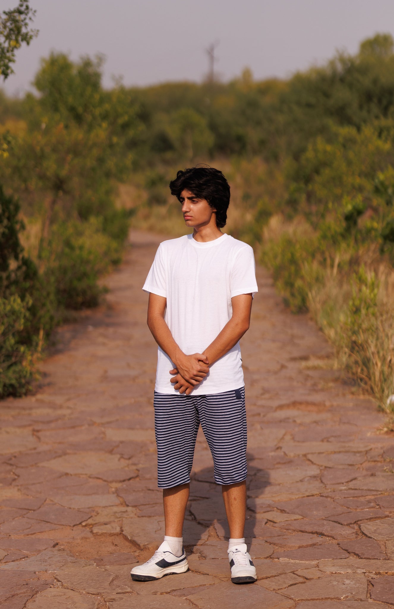 Person standing on a stone path in a natural setting with greenery.