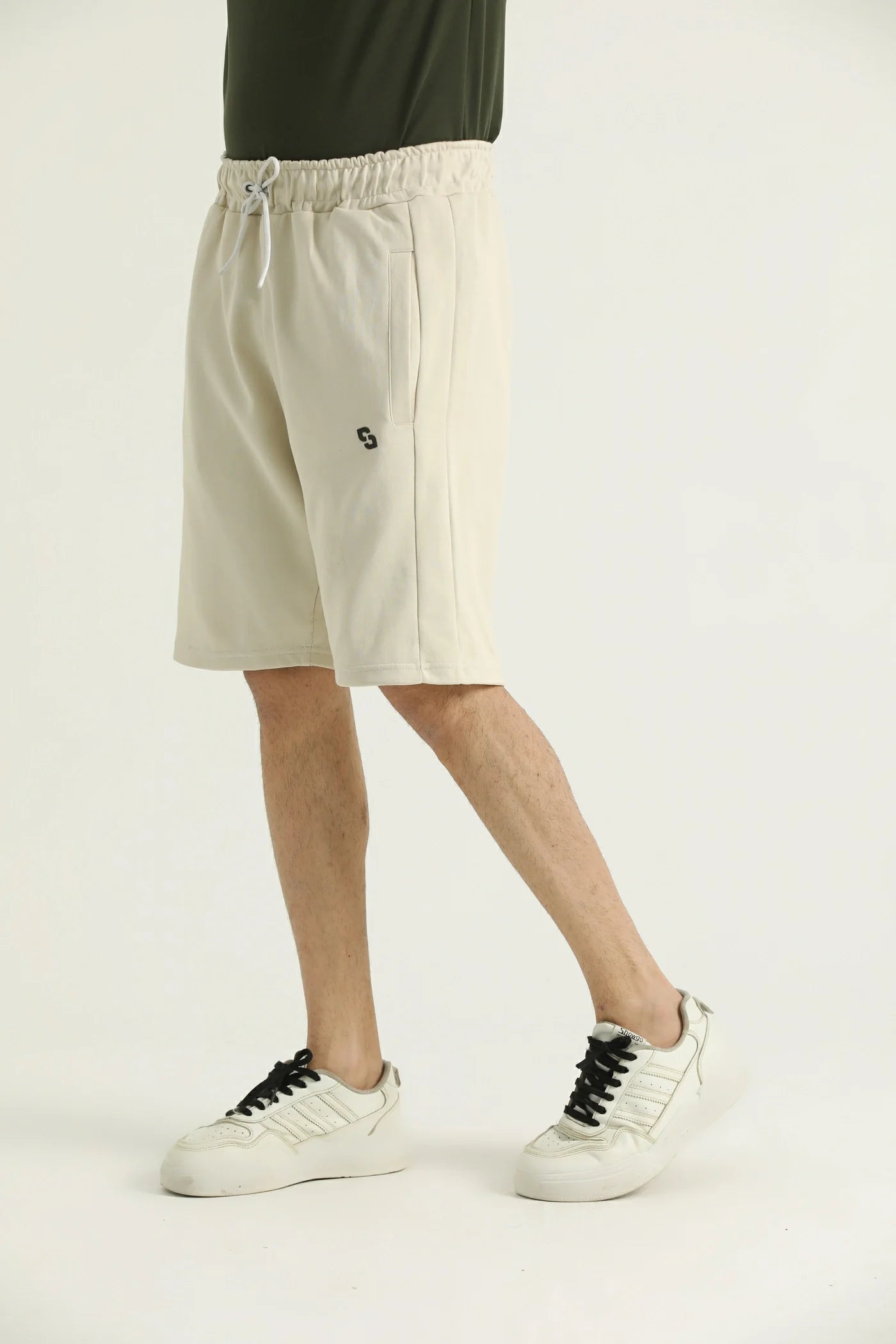 A pair of beige, knee-length shorts with an elasticated waistband and side pockets. Worn with white sneakers.