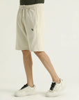 A pair of beige, knee-length shorts with an elasticated waistband and side pockets. Worn with white sneakers.