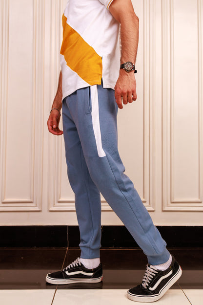 Person wearing blue track pants with a white stripe, white shirt, and black and white sneakers in a room.
