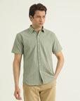 A man wearing a short-sleeved, button-up shirt in green with a collar, chest pocket, and short sleeves.