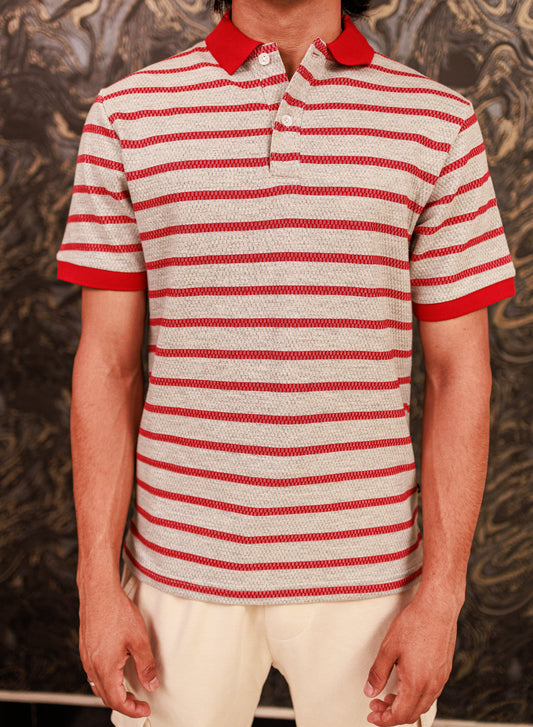 Person wearing a red and white striped polo shirt against a textured wall.
