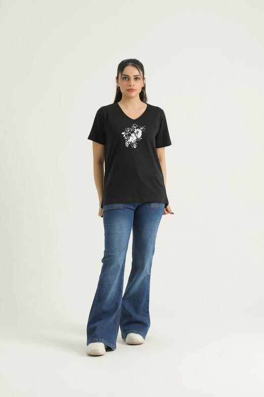 A woman wearing a black V-neck knit tee with a floral print on the front, paired with blue jeans and white shoes.
